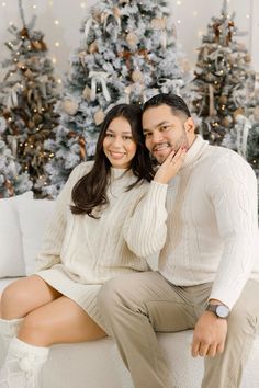 a man and woman sitting on a couch in front of a christmas tree