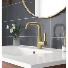 a bathroom sink with a gold faucet next to a mirror and flowers in a vase