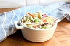 a white bowl filled with coleslaw sitting on top of a wooden table next to a blue towel