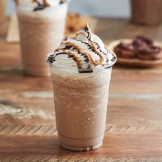 two iced coffees sitting on top of a wooden table next to cookies and milkshakes