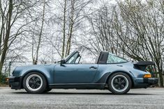 a blue porsche sits parked in front of some trees