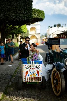 a bride and groom are riding in an old fashioned car on the street with other people