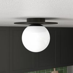 a white light hanging from the ceiling above a kitchen counter top with green tiles on it