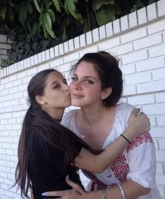 two women are kissing each other in front of a brick wall