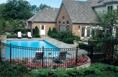 a pool surrounded by flowers and bushes next to a fenced in area with chairs