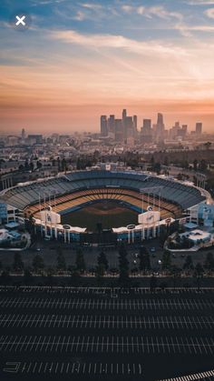 an aerial view of a baseball stadium with the city skyline in the background at sunset