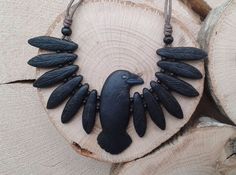 a necklace with black feathers and beads on top of a piece of tree bark in front of some logs