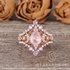 a pink diamond ring sitting on top of a wooden table next to some rose petals