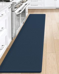 a blue kitchen mat in the middle of a wooden floor with white cabinets and drawers