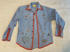 Oh, yes. The quintessential '70s chambray shirt with after-market hand-worked bling! The tag is super-faded, but it says that the shirt is a medium and we are assuming that this "medium" is a women's medium? Check the measurements: 21.5 inches across the chest, armpit to armpit 20.25 inches down the underside of the sleeve, from armpit to hem 31 inches down the back starting at the top of the collar to the hem It feels like 50% polyester / 50% cotton, which was a pretty standard fabric-content of the day, and we can make out the words, "Perma-Prest" on the faded label. In good condition! No holes, rips, stains or other marks! Ready to get back in circulation as your favorite back-to-school shirt this fall! Retro Embroidered Shirt For Spring, Retro Embroidered Blue Top, Retro Blue Embroidered Top, Vintage Embroidered Fall Shirt, Retro Embroidered Button-up Top, Vintage Embroidered Spring Shirt, Retro Embroidered Cotton Shirt, Embroidered Tulips, Work Shirt