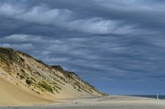 the beach is covered in sand and grass under a cloudy blue sky with white clouds