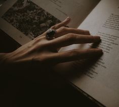 a person's hand on top of an open book with a ring on it