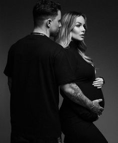 a pregnant woman standing next to a man with tattoos on his arms and chest,