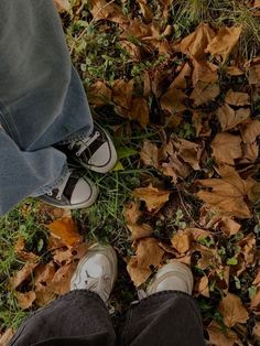 two people standing in the grass with their feet up and leaves on the ground next to them