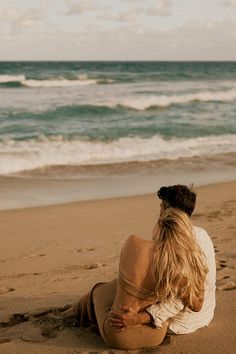 a woman sitting on top of a sandy beach next to the ocean