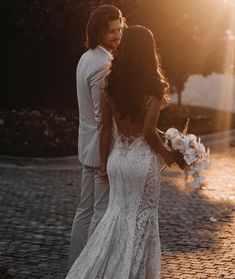 a bride and groom standing together in front of the sun