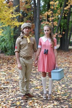 a boy scout and girl scout holding hands in the woods with leaves on the ground