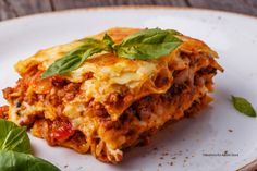 a white plate topped with lasagna covered in sauce and cheese next to a leafy green plant