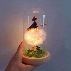 a hand holding a glass dome with miniature figurines in it and lights inside