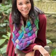 a woman wearing a multicolored knitted scarf sitting on a wooden bench smiling