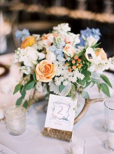 a vase filled with flowers sitting on top of a white table covered in candles and place cards