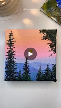 a painting with trees on it and the sun setting in the sky behind it, next to a candle