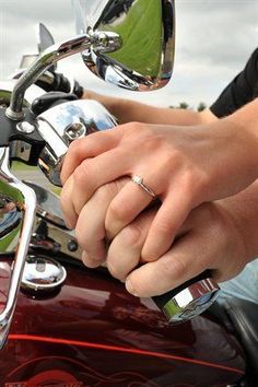 two people holding hands on the handlebars of a motorcycle