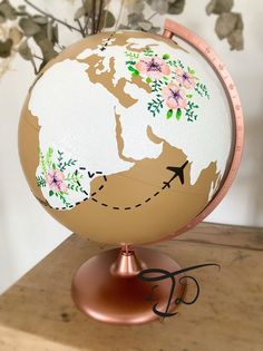 a globe with flowers painted on it sitting on top of a wooden table next to a potted plant