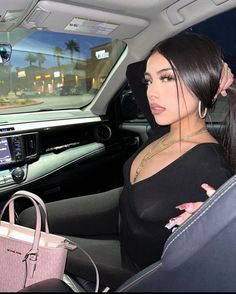 a woman sitting in the back seat of a car holding a pink purse and looking at her cell phone