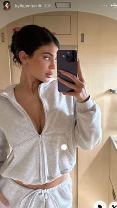 a woman taking a selfie with her cell phone in the bathroom while wearing a gray sweat suit