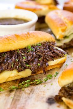 two sandwiches with meat, cheese and sauce sitting on a cutting board next to dipping sauce