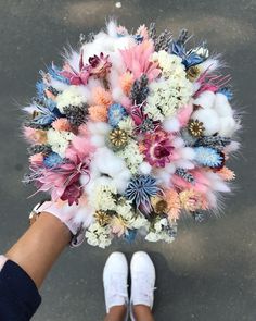 a person holding a bouquet of flowers in their hand with white shoes on the ground