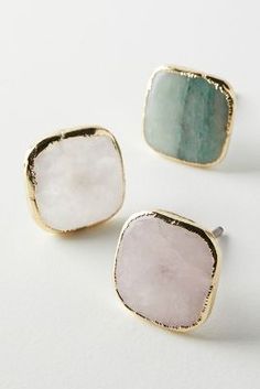 three different colored stone studs on white surface with gold trimming and green accents