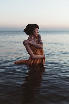 Thoughtful photograph of a woman standing in blue ocean water at dusk wearing an orange dress by Tampa photographer Elle Ione Dress In Water Photoshoot, Moody Beach Photoshoot, Poses In Water, Wild Photoshoot, Photoshoot Cinematic, Lake Portrait, Dusk Dress