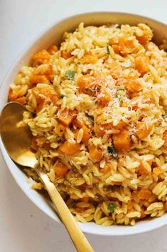 a bowl filled with pasta and carrots on top of a white table next to a gold spoon