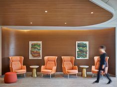 a man walking through an office lobby with orange chairs