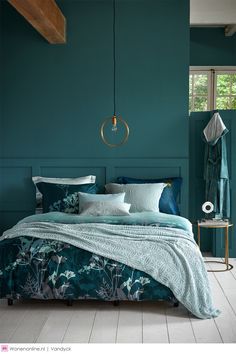 a bedroom with teal walls and bedding in the center, along with a hanging lamp