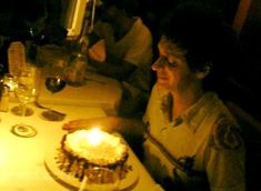 a woman sitting at a table in front of a cake with lit candles on it