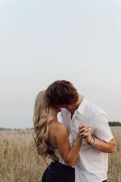 a man and woman are kissing in the middle of an open field with tall grass