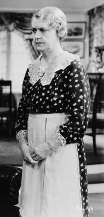 an old black and white photo of a woman standing in a living room with her hands on her hips