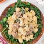 a wooden bowl filled with pasta and spinach on top of a white tablecloth