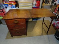 an old wooden desk in a room with other items on the floor and shelves behind it