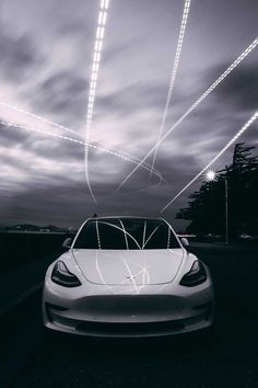 a white car parked on the side of a road at night with lights above it