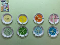 six different colored paper plates on a wall with numbers and fractions cut into them