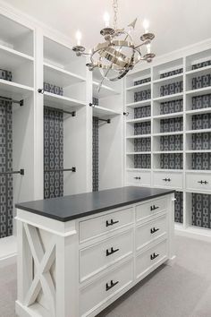 a walk in closet with white cabinets and black counter top, chandelier hanging from the ceiling