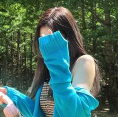 a woman with long brown hair wearing a blue sweater and holding her hand up to her face