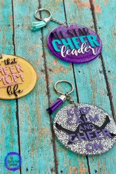 three different colored key chains with the words cheerleader on them, one is purple and one is gold