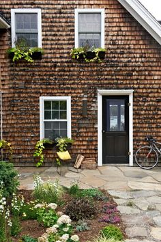 a bicycle is parked in front of a brick building with two windows and plants growing on the side