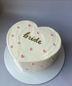 a white heart shaped cake with pink hearts on it and the word bride spelled in gold