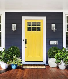 a yellow door is on the front of a blue house with white planters and potted plants